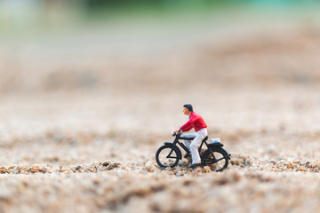 Miniature people : Travellers riding a bicycle  on The sand