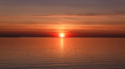 Beautiful sunset over the sea. The sun sets on the water. The sky is painted with bright colors. Sunset beach in a summer evening. Gulf of Finland, Baltic sea, Kronstadt, Saint-Petersburg, Russia.