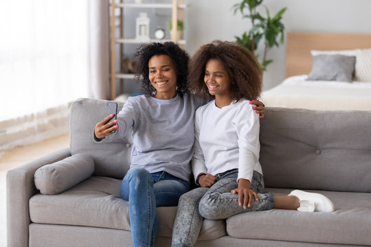 Smiling African American mother and daughter taking selfie at home