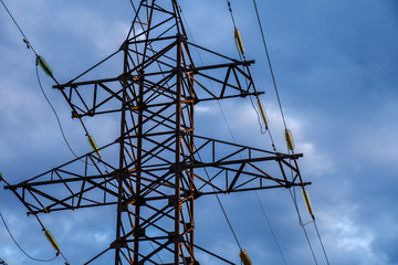 High voltage power pylons against blue sky and sun