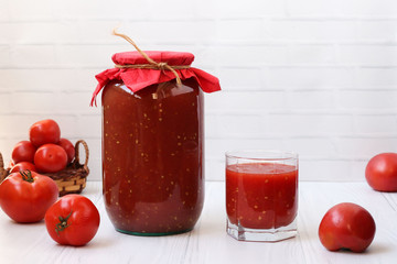 Tomato juice in cans and in a glass is on the table on a white background