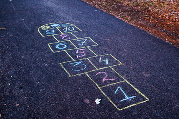 Hopscotch game being drawn with a chalk on the asphalt ground as seen from above