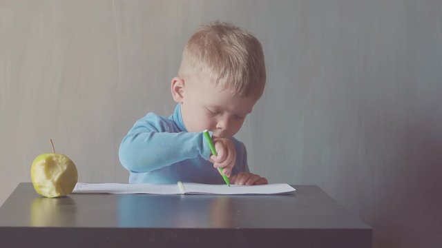 two year old boy is drawing with marker at album and eating apples