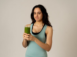Beautiful young sports latin woman boring of diet holding green smoothie in dislike