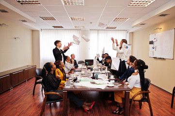 Multiracial business team meeting around boardroom table, two team leaders throw paper up.
