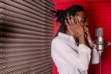 African musician standing in headphones singing into a microphone in a recording Studio