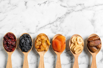 Spoons of different dried fruits on marble background, top view with space for text. Healthy...