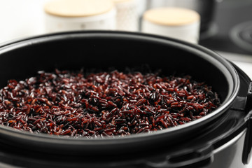 Modern multi cooker with boiled brown rice in kitchen, closeup