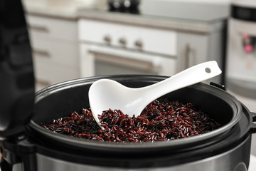 Modern multi cooker with spoon and boiled brown rice in kitchen, closeup