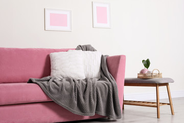 Fototapeta na wymiar Cozy living room interior with sofa, pillows and plaid near light wall