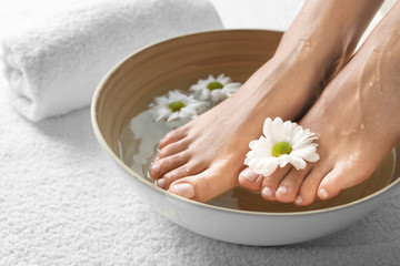 Obraz na płótnie Canvas Closeup view of woman soaking her feet in dish with water and flowers on white towel. Spa treatment