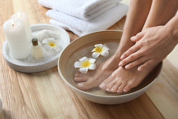 Obraz na płótnie Canvas Closeup view of woman soaking her feet in dish with water and flowers on wooden floor. Spa treatment