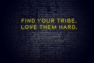 Neon sign with positive wise motivational quote against brick wall 