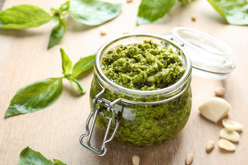 Jar of tasty pesto sauce on table, closeup