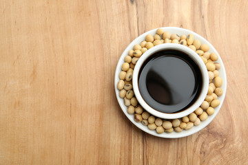 Dish of soy sauce with beans on wooden background, top view. Space for text