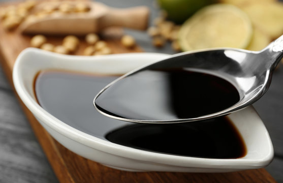Spoon with soy sauce over dish, closeup