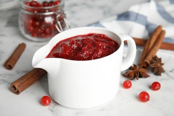 Pitcher of cranberry sauce and spices on marble table, closeup
