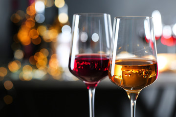 Glasses with different wines against defocused lights, closeup. Space for text