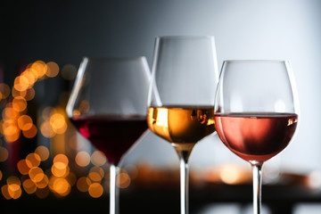 Glasses with different wines against defocused lights, closeup. Space for text