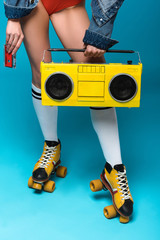 cropped view of woman in swimsuit and roller skates holding boombox and cassette tape on blue