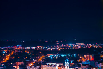 Fototapeta premium Landscape of city at nighttime with buildings and streets in a blue and violet neon light - Top scene of a town with modern architecture – Concept image for night life and travel