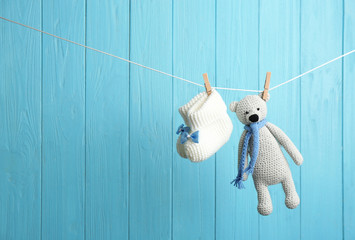 Baby booties and toy bear on laundry line against color wooden background, space for text. Child accessories