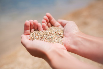 Sign of love for the sea, the heart of sand in female hands. Sandy beach and blue water in summer. Vacation and tourism concept