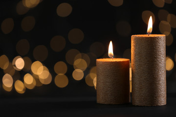 Burning gold candles against blurred lights in darkness. Space for text