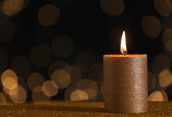 Burning gold candle on table against blurred lights. Space for text