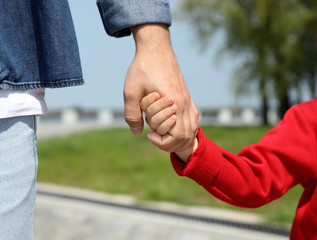 Little child holding hands with his father  outdoors, closeup. Family weekend