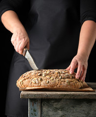 female hands hold oval baked rye bread with pumpkin seeds
