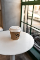 Close up composition of paper hot coffee cup on white metal table setting near glass window in natural light scene / coffee shop concept / nice composition background / background for advertising