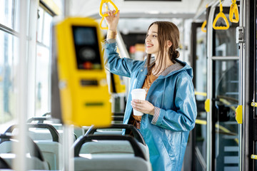 Young woman passenger enjoying trip at the public transport, standing with coffee in the modern tram