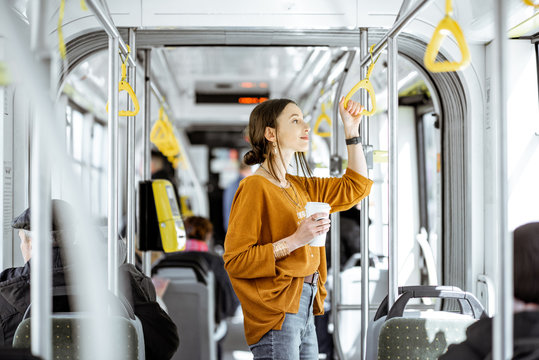 Young woman passenger enjoying trip at the public transport, standing with coffee in the modern tram