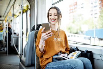 Young and happy woman using smartphone while sitting near the window in the public transport during...