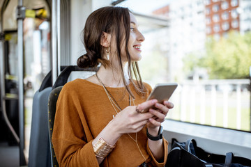 Young and happy woman using smartphone while sitting near the window in the public transport during...