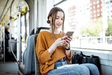 Young and happy woman using smartphone while sitting near the window in the public transport during...