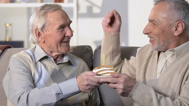 Senior man presenting birthday cake with candle, friendship connection, surprise
