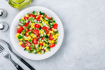 Fresh summer corn salad bowl with tomatoes, cucumbers, red onions and parsley.