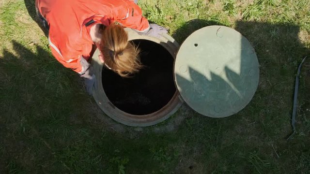 Girl plumber looks into an open draining manhole. top view. Service of the house individual sewerage.