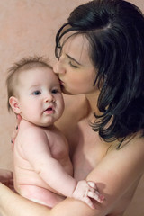 Young beautiful mother brunette without clothes holding her arms and kissing her little son