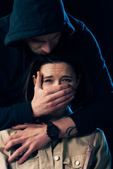 partial view of criminal attacking scared woman and covering her mouth isolated on black