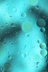 Drops of oil in water on a colored background. Bright background with blue-green circles of different sizes. Blurred, vertical, place for text, monophonic. Design concept.