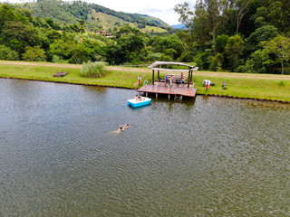 Fototapeta premium Aerial view of beautiful little wood cabana next the lake in tropical mountain, with family enjoying relax sun moment, swimming and fishing. Monte Alegre Do Sul, Brazil. 