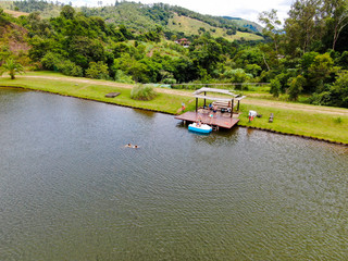 Fototapeta premium Aerial view of beautiful little wood cabana next the lake in tropical mountain, with family enjoying relax sun moment, swimming and fishing. Monte Alegre Do Sul, Brazil. 