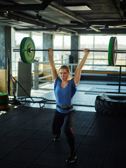 Obraz na płótnie Canvas Strong female athlete wearing weightlifting belt doing clean and jerk exercise with barbell during cross training in gym