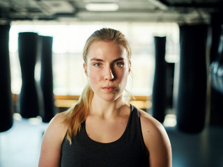 Fototapeta na wymiar Portrait of beautiful athletic woman looking at camera standing among boxing bags in gym and feeling confident.