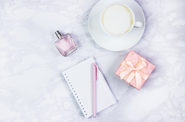 Women's accessories on a white marble table. Notepad, pen and glass of coffee on the table and other female cosmetic accessories. Beauty and fashion concept. Top view, flat lay, copy space