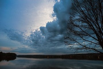 Tree silhouette against the evening sky with clouds over the lake.