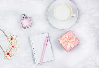 Women's accessories on a white marble table. Notepad, pen and glass of coffee on the table and other female cosmetic accessories. Beauty and fashion concept. Top view, flat lay, copy space